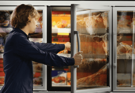 Man is opening a freezer for ready meals in a supermarket and the reflection shows cows